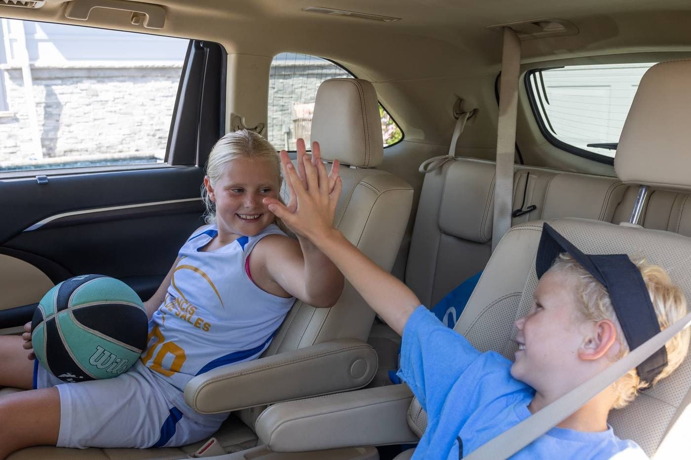 Two kids high-fiving in the back seat of a car